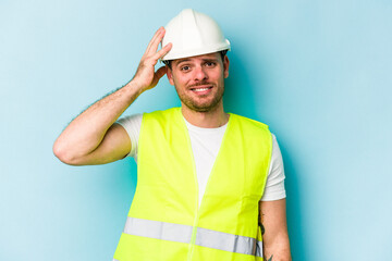 Young laborer caucasian man isolated on blue background being shocked, she has remembered important meeting.
