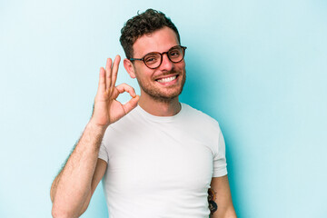 Young caucasian man isolated on blue background cheerful and confident showing ok gesture.