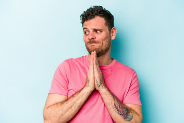 Young caucasian man isolated on blue background praying, showing devotion, religious person looking...