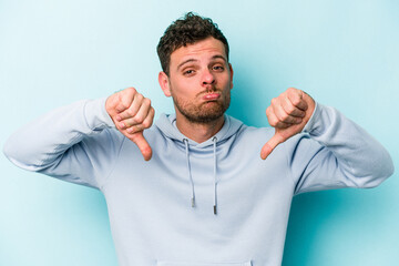 Young caucasian man isolated on blue background showing a dislike gesture, thumbs down....