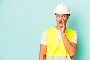 Young laborer caucasian man isolated on blue background is saying a secret hot braking news and looking aside