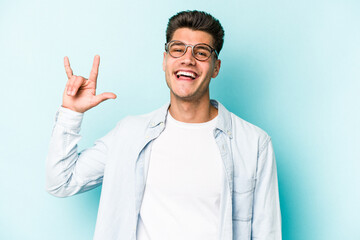 Young caucasian man isolated on blue background showing a horns gesture as a revolution concept.