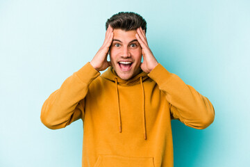 Young caucasian man isolated on blue background receiving a pleasant surprise, excited and raising hands.