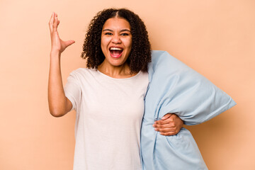 Young African American woman holding a pillow isolated on beige background receiving a pleasant...