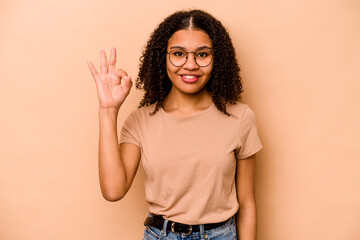 Young African American woman isolated on beige background cheerful and confident showing ok gesture.