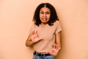 Young African American woman isolated on beige background rejecting someone showing a gesture of...