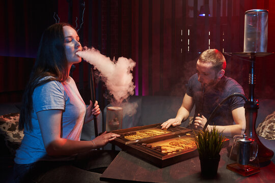young couple smoking hookah in atmospheric hookah bar. sit freely on sofas, play backgammon and emit white smoke