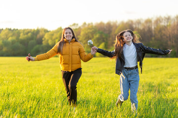 Mom and daughter casual dressed run in field at beautiful spring sunset.