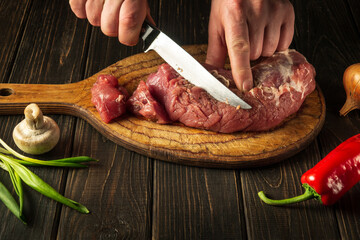 Close-up of a chef hands cutting raw veal meat on a cutting board before cooking. Peasant foods.