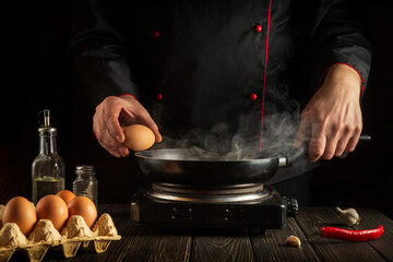 The chef tries to break an egg on a frying pan to make delicious breakfast. Working environment in the kitchen. Menu idea for a restaurant or hotel