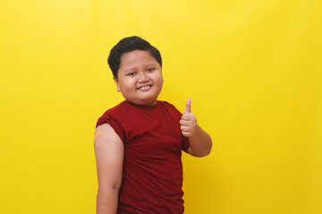 Asian boy with vaccine sleeve standing and showing thumbs up. Isolated on yellow background