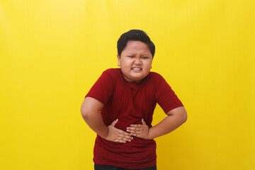 Asian boy standing holding stomach feeling pain. Healthcare concept. Isolated on yellow background