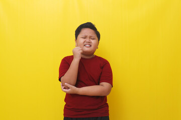 Asian boy feel pain in the elbow. Healthy concept. Isolated on yellow background