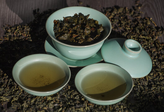 Gaivan and bowls with green tea and tea leaves on a brown background close-up, selective focus. Tea ceremony. Traditional Chinese tea ware.