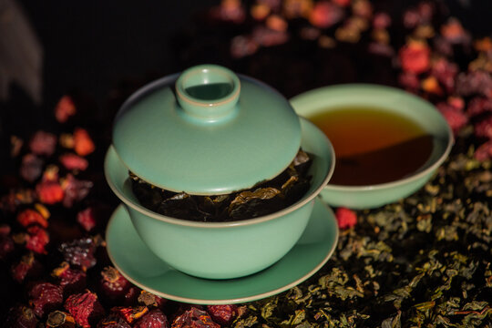 Gaivan and bowls with green tea and tea leaves on a brown background close-up,selective focus. Tea ceremony. Traditional Chinese tea ware.Gaiwan cup.Zhu yao ceramic.Chinese ceramics.Blurred defocused.