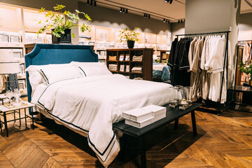 View of assortment of decor for interior shop in store of shopping center. View of bed with linen, bed linen, pillows, plaid. View of home accessories for bedroom in shop fashion retail store. Home