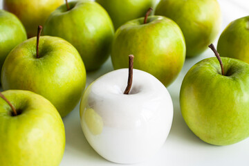 Many bright green apples and one white ceramic lie on a white uniform background. Conceptual photo.