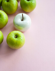 Many bright green apples and one white ceramic lie on a pink uniform background. Conceptual photo.