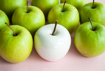 Many bright green apples and one white ceramic lie on a pink uniform background. Conceptual photo.