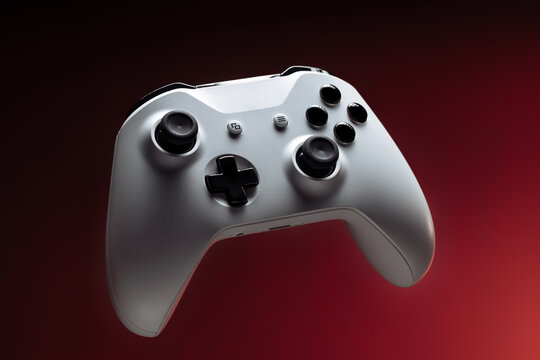 Modern white gamepad, on a red red background. Game controller for video games and sports on a dark red background.