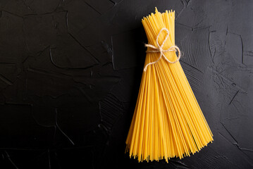 Dry pasta spaghetti with black ribbon over black textured background - obrazy, fototapety, plakaty