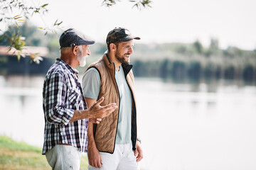 Senior father and his adult son talking by the lake in nature.