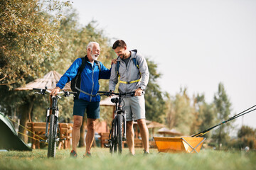 Happy man and his senior father talk while preparing for bicycle riding in nature.