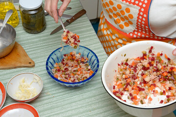 Hands of woman that transferring Russian salad to plastic bowl.