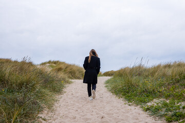 Woman with long hair walking in the sand on a path in the dunes near the beach