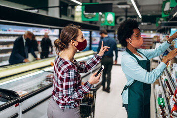 Young woman with face protective mask is buying groceries at the supermarket and talking with emloyee. Covid-19, Coronavirus, newnormal concept.