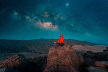 man sitting on the top of the mountain meditating at night with Milky Way background.