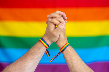 Pareja con las manos unidas y con pulseras con la bandera lgtbi , sobre fondo con la bandera del...