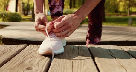 Woman tying running shoes in the park outdoor, female runner ready for jogging on the road outside