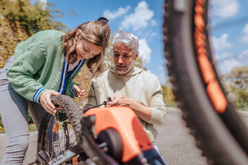 Obraz premium Happy father with teenage daughter repairing bicycle in street in town.