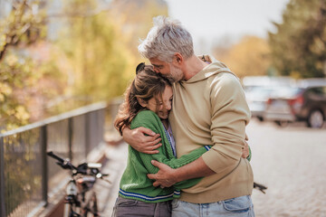 Teenage daughter hugging her father outside in town when spending time together. - obrazy, fototapety, plakaty