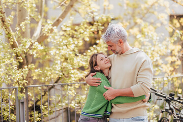 Teenage daughter hugging her father outside in town when spending time together.