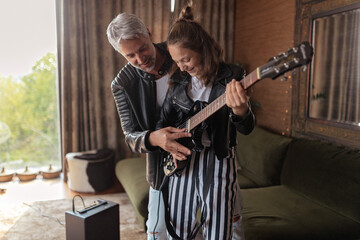 Father learning his teenage daughter to play the electric guitar at home.