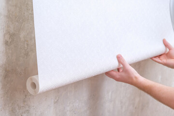 A man rolls out a roll of white wallpaper on the wall with glue. Wallpapering. Repair of a room,...