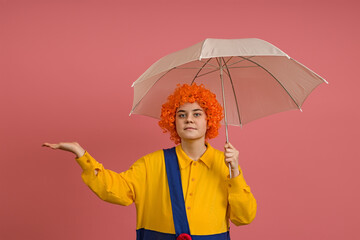 clown girl in a wig and a yellow-blue suit with an umbrella on a colored background