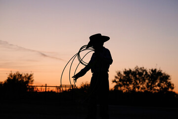 Young cowboy with rope in Texas sunset on ranch for childhood western lifestyle. - obrazy, fototapety, plakaty