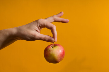 female hand holding a red apple on a yellow background