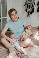 Happy young mother holding two twin babies in bed at home