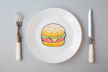 A painted hamburger lies on a white plate next to a knife and fork on a gray background. The topic of sanction and the closure of fast food restaurants. View from the top point.