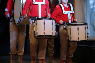 A group of young musicians in red military uniform with percussion musical instruments playing...
