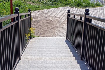 gray concrete steps on the stairs with black iron handrails near the sidewalk in the park