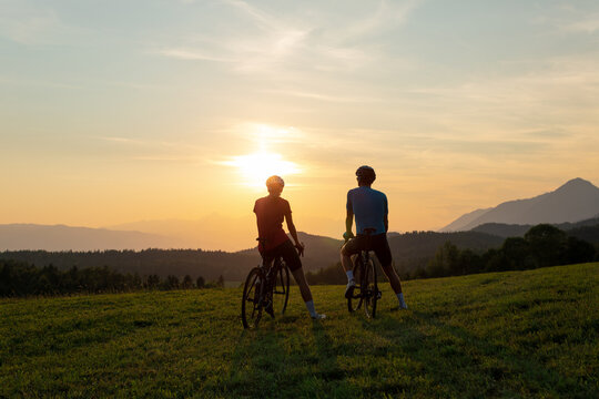 Woman and man, road racing bikers, sitting on bicycles, enjoying a beautiful mountain landscape at sunset