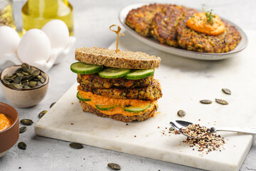 A healthy gluten-free sandwich: homemade power bread, quinoa and carrot fritter, orange bell pepper hummus, cucumbers, sunflower seeds on marble board