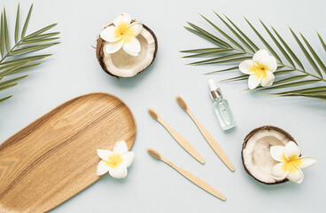 Fototapeta na wymiar Bamboo toothbrush and bootle essential oil on a table with copy space on a white background. Styled composition of flat lay with coconut, tropical leaves and flowers.
