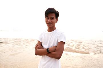 Asian young man with the arms crossed wearing a digital bacelet on a beach