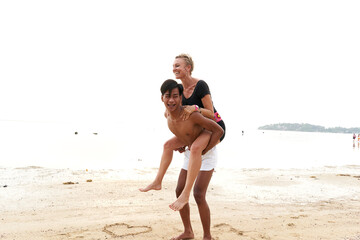 Fototapeta na wymiar Asian man piggyback riding to a his couple in a sandy tropical beach